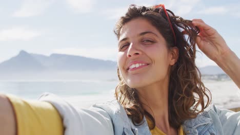 Fröhliche-Frau-Mit-Gemischter-Abstammung,-Die-Ein-Selfie-Video-Macht-Und-Auf-Der-Sonnigen-Promenade-Am-Meer-Winkt-Und-Lächelt
