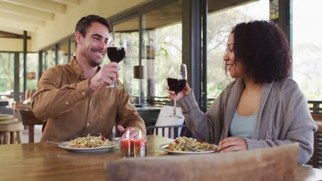 Mixed-race-couple-toasting-and-drinking-wine-while-having-lunch-at-a-restaurant