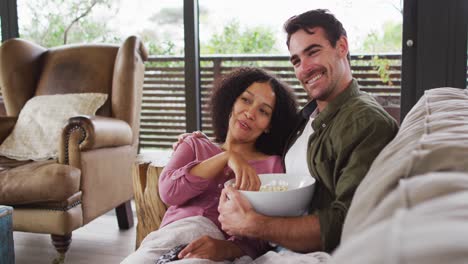 Smiling-mixed-race-couple-eating-popcorn-while-watching-a-movie-together-at-vacation-home