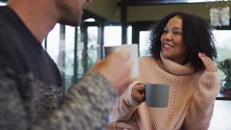 Happy-diverse-couple-talking-and-drinking-coffee-in-kitchen