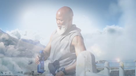 Animation-of-glowing-lights-over-fit-senior-man-drinking-water-during-exercise-and-clouds-background
