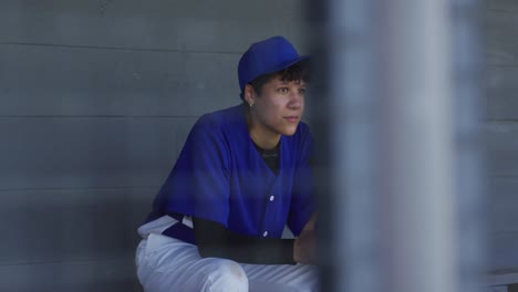 Nervöse-Gemischtrassige-Baseballspielerin,-Die-Auf-Einer-Bank-Sitzt-Und-Wartet-Und-Einen-Baseballball-Hält
