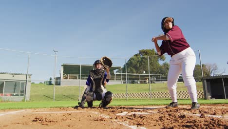 Diverse-group-of-female-baseball-players-playing-on-the-field,-hitter-swinging-for-pitched-ball