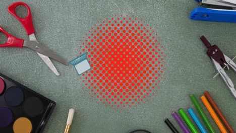 Animation-of-laptop-and-schoolbag-bouncing-on-red-dots-over-desk-with-stationery