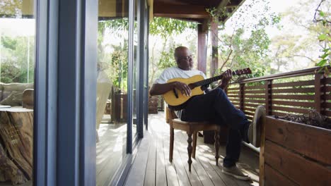 Nachdenklicher-Afroamerikanischer-älterer-Mann,-Der-Auf-Dem-Balkon-Sitzt-Und-Akustikgitarre-Spielt