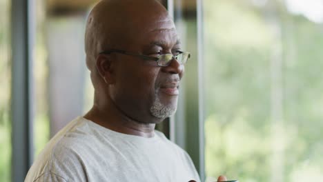 Thoughtful-african-american-senior-man-drinking-mug-of-coffee-and-smiling