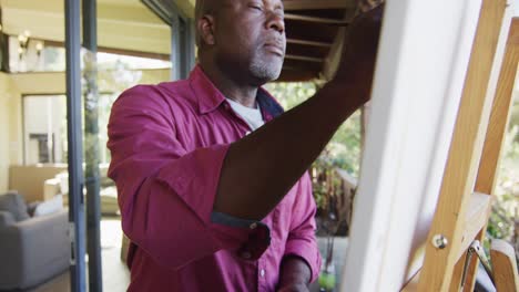 Happy-african-american-senior-man-standing-on-balcony-painting-picture-on-canvas