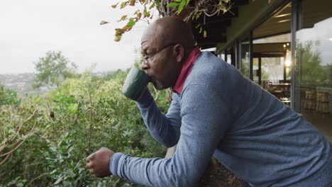 Afroamerikanischer-älterer-Mann,-Der-Auf-Dem-Balkon-Steht,-Kaffee-Trinkt-Und-Die-Aussicht-Betrachtet