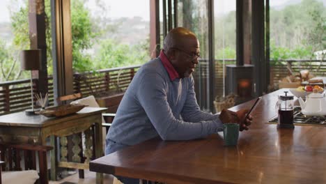 Afroamerikanischer-älterer-Mann-Sitzt-Mit-Smartphone-In-Der-Küche-Und-Trinkt-Kaffee