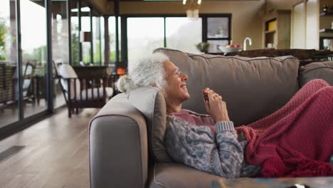 Senior-mixed-race-woman-lying-on-sofa-using-tablet