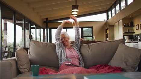 Senior-mixed-race-woman-sitting-on-sofa-celebrating