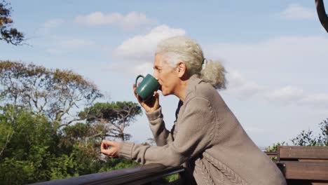 Portrait-of-senior-mixed-race-woman-holding-mug-and-drinking-on-balcony