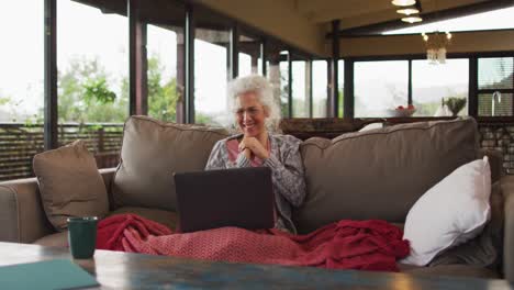 Senior-mixed-race-woman-sitting-on-sofa-having-video-call-using-laptop