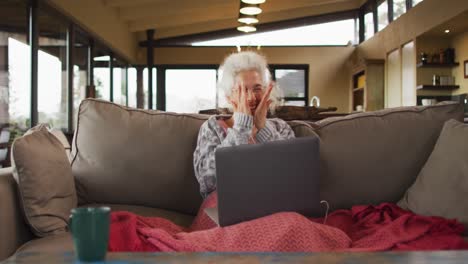 Senior-mixed-race-woman-sitting-on-sofa-having-video-call-using-laptop