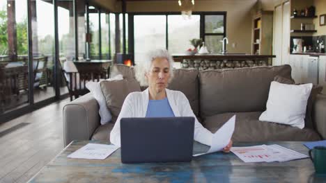 Senior-mixed-race-woman-sitting-on-sofa-using-laptop