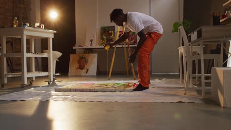 Artista-Masculino-Afroamericano-Vertiendo-Pintura-Sobre-Lienzo-Y-Pintando-En-Un-Estudio-De-Arte.