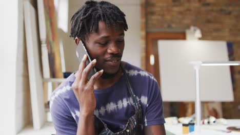 Smiling-african-american-male-painter-talking-on-smartphone-in-artist-studio