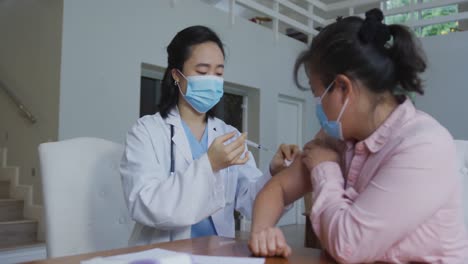 Asian-female-nurse-wearing-face-mask-giving-covid-vaccination-to-female-patient-in-hospital