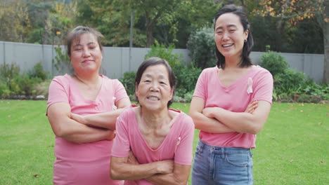 Portrait-of-smiling-asian-adult-granddaughter,-mother-and-grandmother-standing-in-garden-smiling