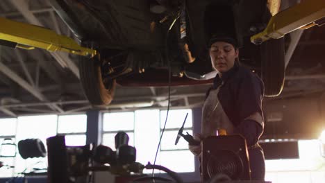 Female-mechanic-wearing-welding-helmet-working-under-a-car-at-a-car-service-station