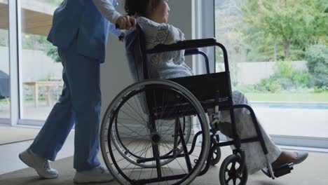 Asiatische-Ärztin-Schiebt-Patientin-Im-Rollstuhl-Im-Krankenhaus