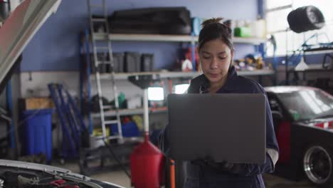 Mecánica-Femenina-Usando-Una-Computadora-Portátil-E-Inspeccionando-El-Automóvil-En-Una-Estación-De-Servicio-De-Automóviles