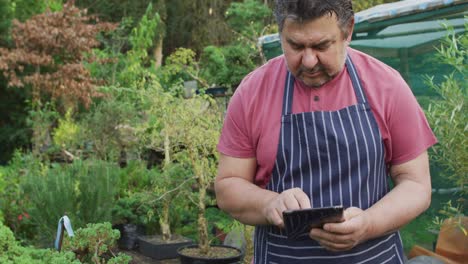 Caucasian-male-gardener-checking-tree-and-using-tablet-at-garden-center