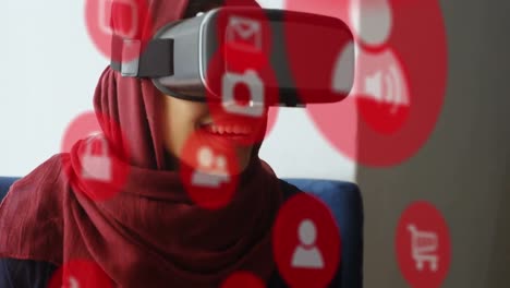 Multiple-red-digital-icons-floating-against-businesswoman-in-hijab-wearing-vr-headset-at-office