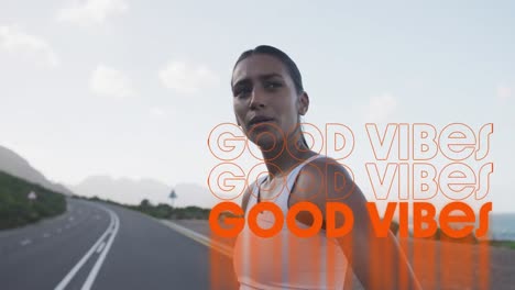 Animation-of-the-words-good-vibes-written-in-orange-over-woman-exercising-standing-on-mountain-road