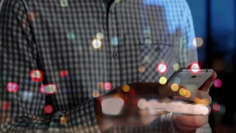 Spots-of-colorful-bokeh-lights-against-mid-section-of-man-using-smartphone-on-the-street