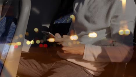 Flecken-Von-Bokeh-Lichtern-Vor-Dem-Mittelteil-Eines-Mannes,-Der-In-Einem-Bus-Sein-Smartphone-Benutzt