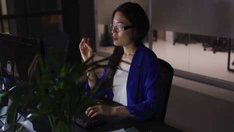 Video-of-tired-asian-businesswoman-in-glasses-sitting-at-desk-working-at-night-in-office