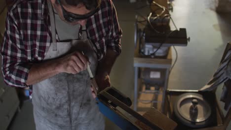 Caucasian-male-knife-maker-in-workshop-wearing-glasses-and-using-sander