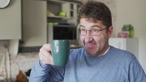 Smiling-and-relaxed-caucasian-man-drinking-coffee-in-kitchen-at-home