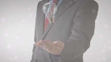 Animation-of-media-icons-floating-over-midsection-of-businessman-throwing-and-catching-lightbulb