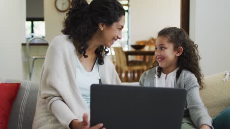 Happy-mixed-race-mother-and-daughter-sitting-on-the-sofa,having-fun-and-using-laptop