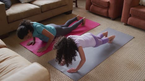 Mixed-race-mother-and-daughter-practicing-yoga-in-living-room