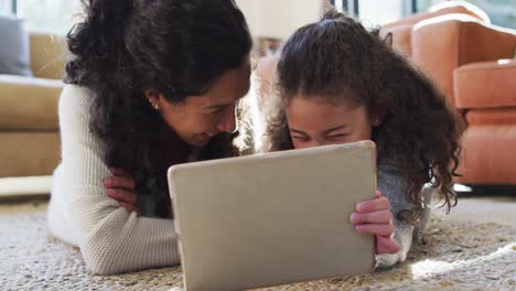 Happy-mixed-race-mother-and-daughter-laying-on-the-floor,having-fun-and-using-tablet