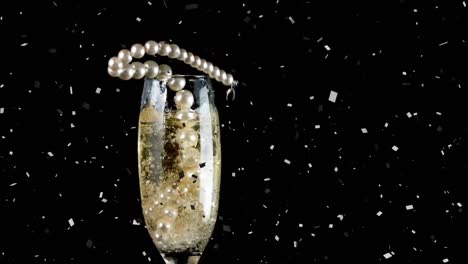 Animation-of-confetti-and-pearl-necklace-falling-into-glass-of-champagne-on-black-background