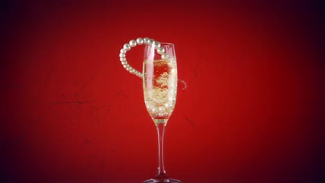 Animation-of-pearl-necklace-falling-into-glass-of-champagne-on-red-background