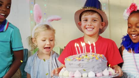 Animation-of-confetti-falling-over-boy-holding-birthday-cake-at-children's-party
