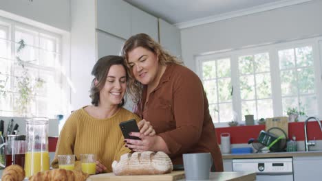 Caucasian-lesbian-couple-sitting-at-table-using-smartphone