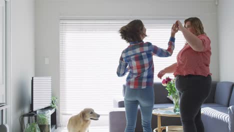 Caucasian-lesbian-couple-dancing-and-smiling-with-dog