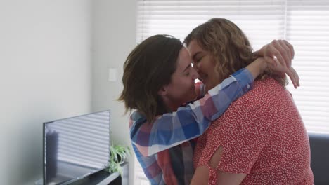 Caucasian-lesbian-couple-embracing-and-kissing-in-living-room