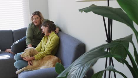 Caucasian-lesbian-couple-smiling-and-sitting-on-couch-with-dog
