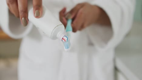 Mid-section-view-of-mixed-race-woman-putting-toothpaste-on-toothbrush