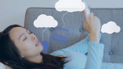 Animation-Von-Wolken-Und-Mediensymbolen-über-Einer-Frau,-Die-Ihr-Smartphone-Nutzt