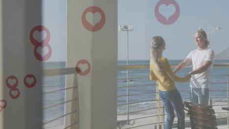 Multiple-red-heart-icons-floating-against-caucasian-couple-dancing-in-the-balcony