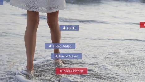 Animation-of-social-media-notifications-over-legs-of-woman-on-holiday-paddling-in-the-sea