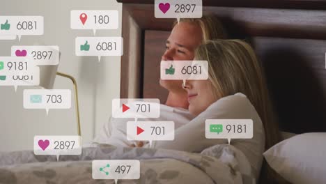 Animation-of-social-media-notifications-over-smiling-couple-relaxing-in-bed-embracing
